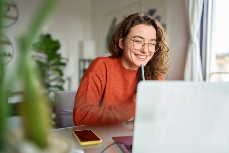 A female college student sitting in a dorm room, using a laptop to calculate a monthly college budget spreadsheet.